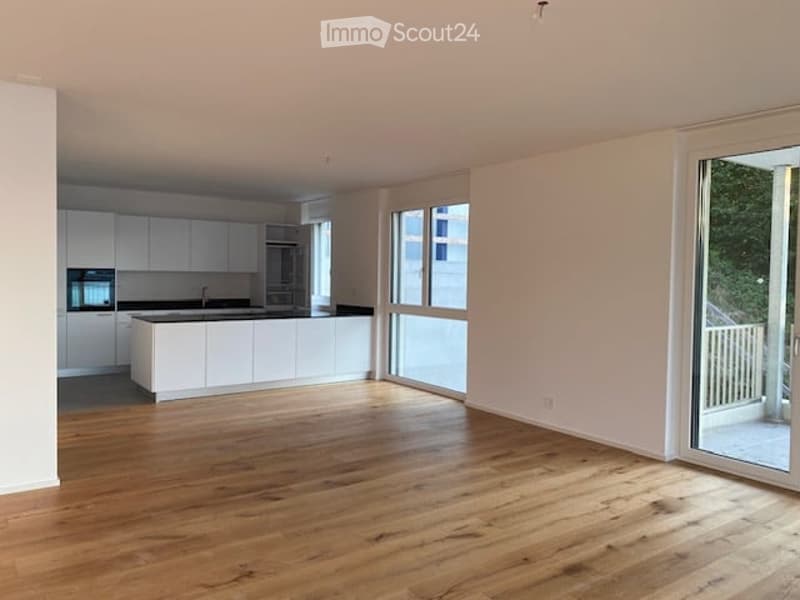 Open-plan living and kitchen area with light wood flooring, white cabinetry, and large windows leading to a balcony.