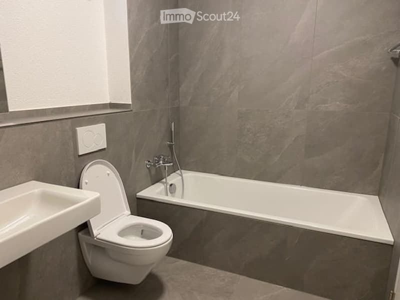 Modern bathroom with grey stone walls, white bathtub, toilet, and sink.