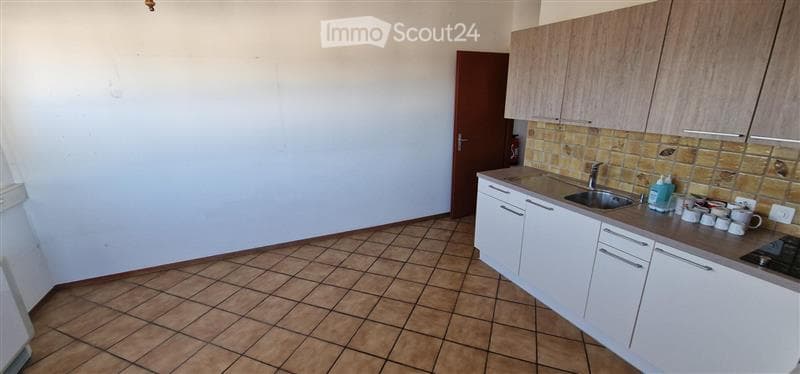 Modern kitchen with white cabinets, tiled backsplash, and a tiled floor. Features a sink, faucet, stove, and several cups on the counter.