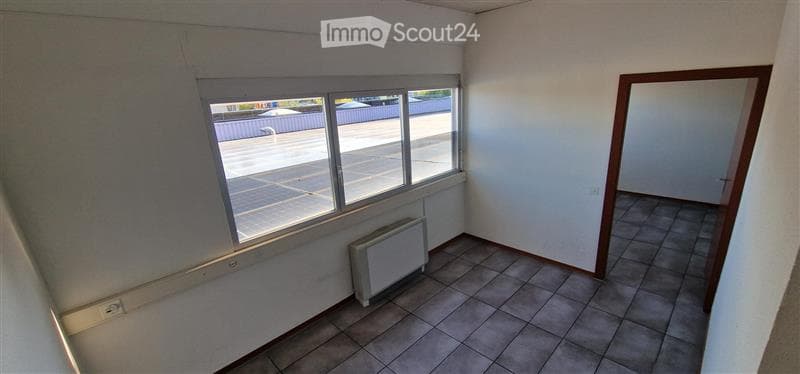 Empty room with tiled floor, white walls, large windows, radiator, and a door leading to another space.