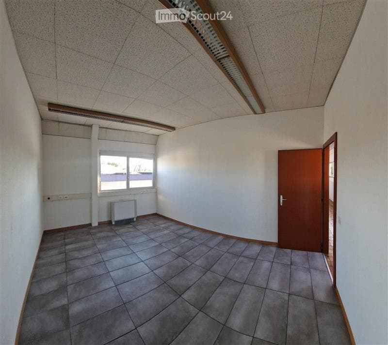 Empty room with grey tiled floor, white walls, and a single window. There is a radiator under the window and a wooden door on the right side.
