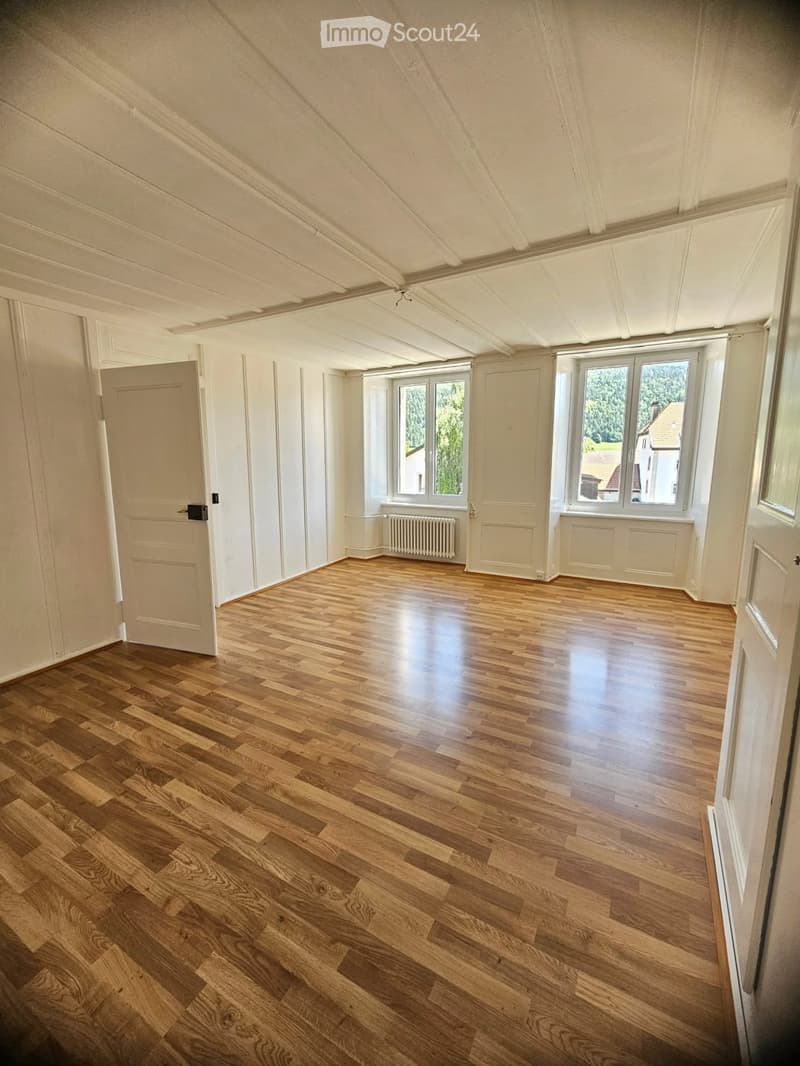 Empty room with wooden flooring, white walls, large windows, and a radiator. No furniture or equipment present.