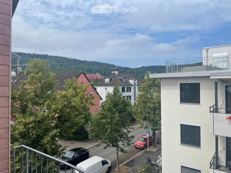 Balcony view overlooking a residential street with parked cars, trees, and neighboring houses.
