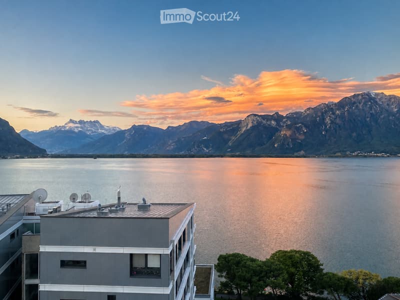 Modern building with a panoramic view of a lake and mountain range at sunset.