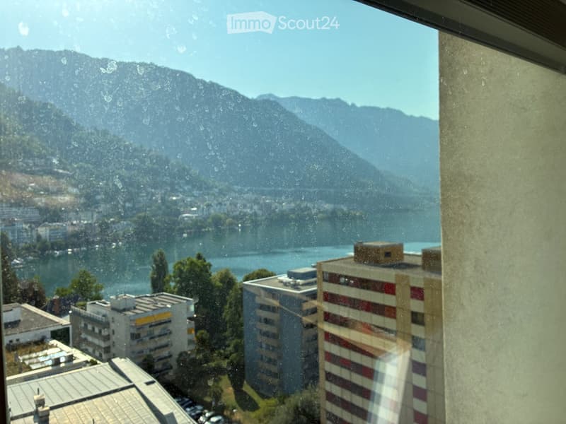 View from a balcony showing a lake, mountains, and surrounding buildings.