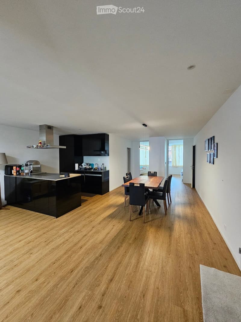 Open-plan kitchen and dining area with wooden flooring, black kitchen island, dining table with chairs, and modern cabinets.
