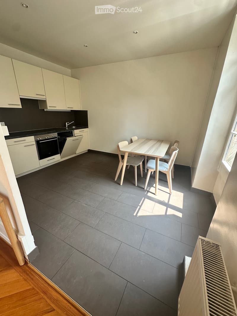 Modern kitchen with white cabinets, black countertops, and a dining area with a table and chairs.