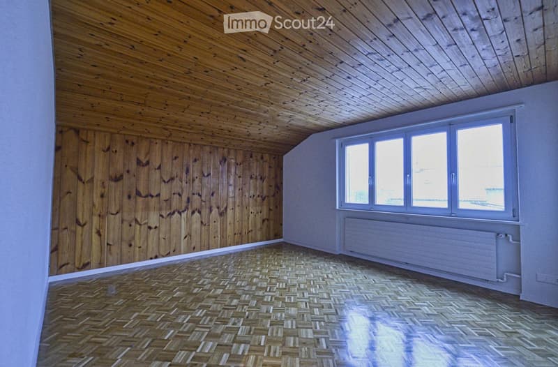 Empty room with wooden walls, herringbone wooden floor, and large windows with white frames. No furniture or equipment present.