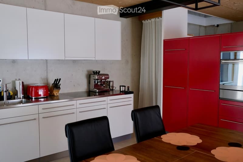 Modern kitchen with white and red cabinets, stainless steel appliances, a wooden dining table with chairs, and various kitchen items on the counter.