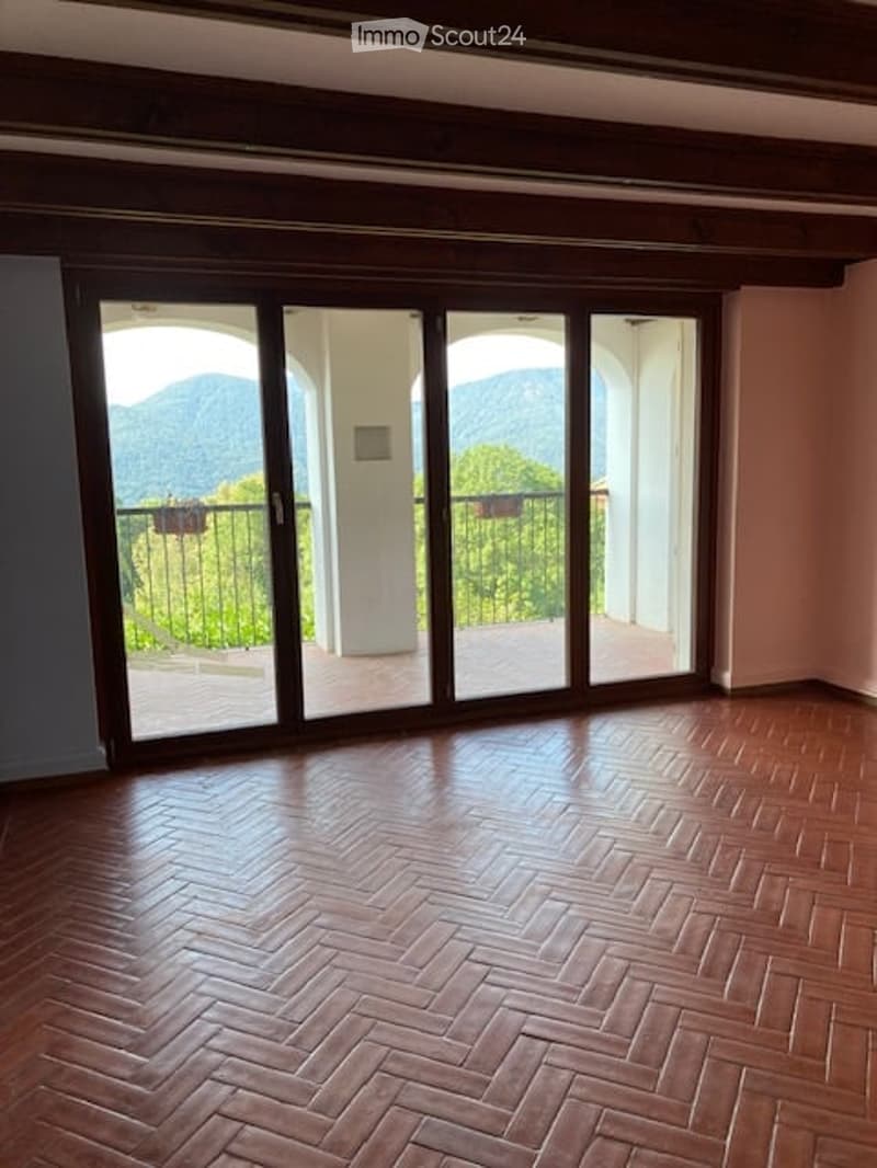 Empty room with wooden herringbone flooring and large sliding glass doors opening to a balcony with a scenic mountain view.