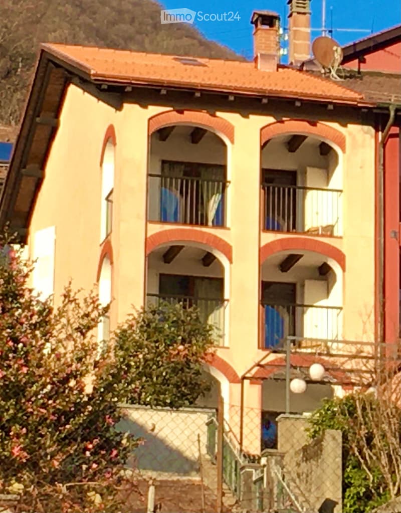 Two-story yellow house with red brick accents, arched windows, balconies, and a satellite dish on the roof.