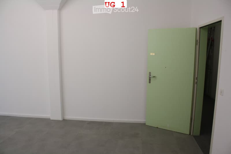 Empty room with white walls, grey tiled floor, and a green door leading to another space.