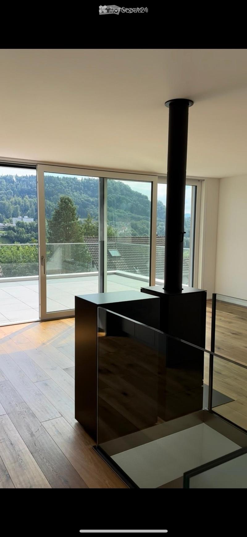 Modern living space with wooden flooring, large glass doors leading to a balcony, and a sleek black fireplace.