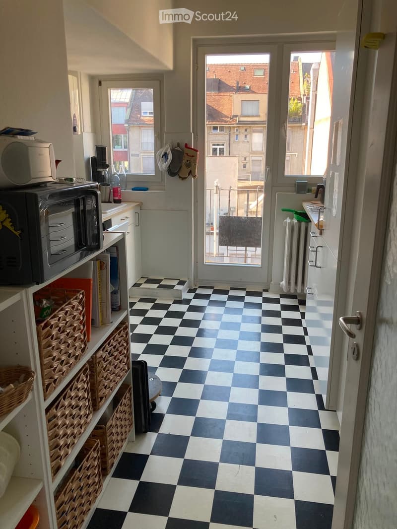 Kitchen with black and white checkered floor, microwave, fridge, oven, sink, radiator, shelves with wicker baskets, and a door leading to a balcony.