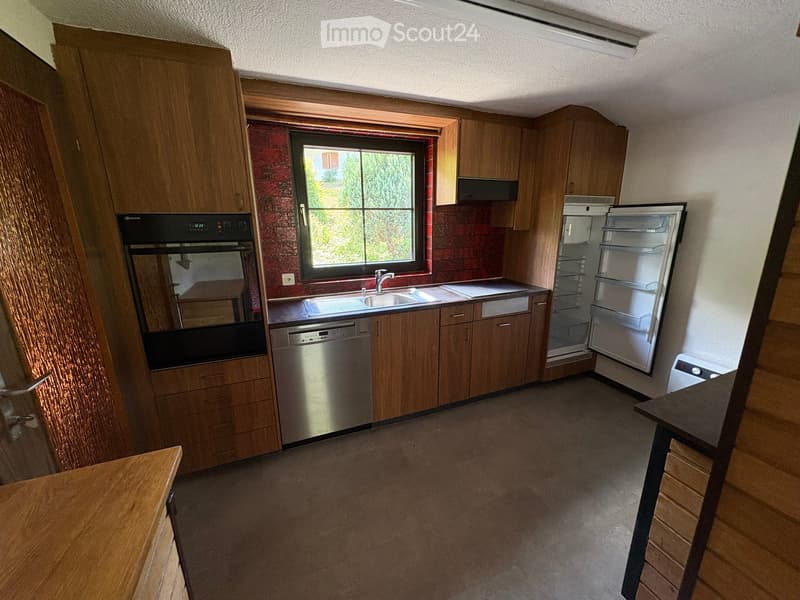 Modern kitchen with wooden cabinets, stainless steel appliances, and a large window overlooking greenery.