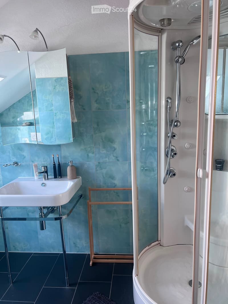 Modern bathroom with a white sink, glass shower enclosure, bathtub, and blue mosaic tiles. Includes a mirror, towel, and toiletries.