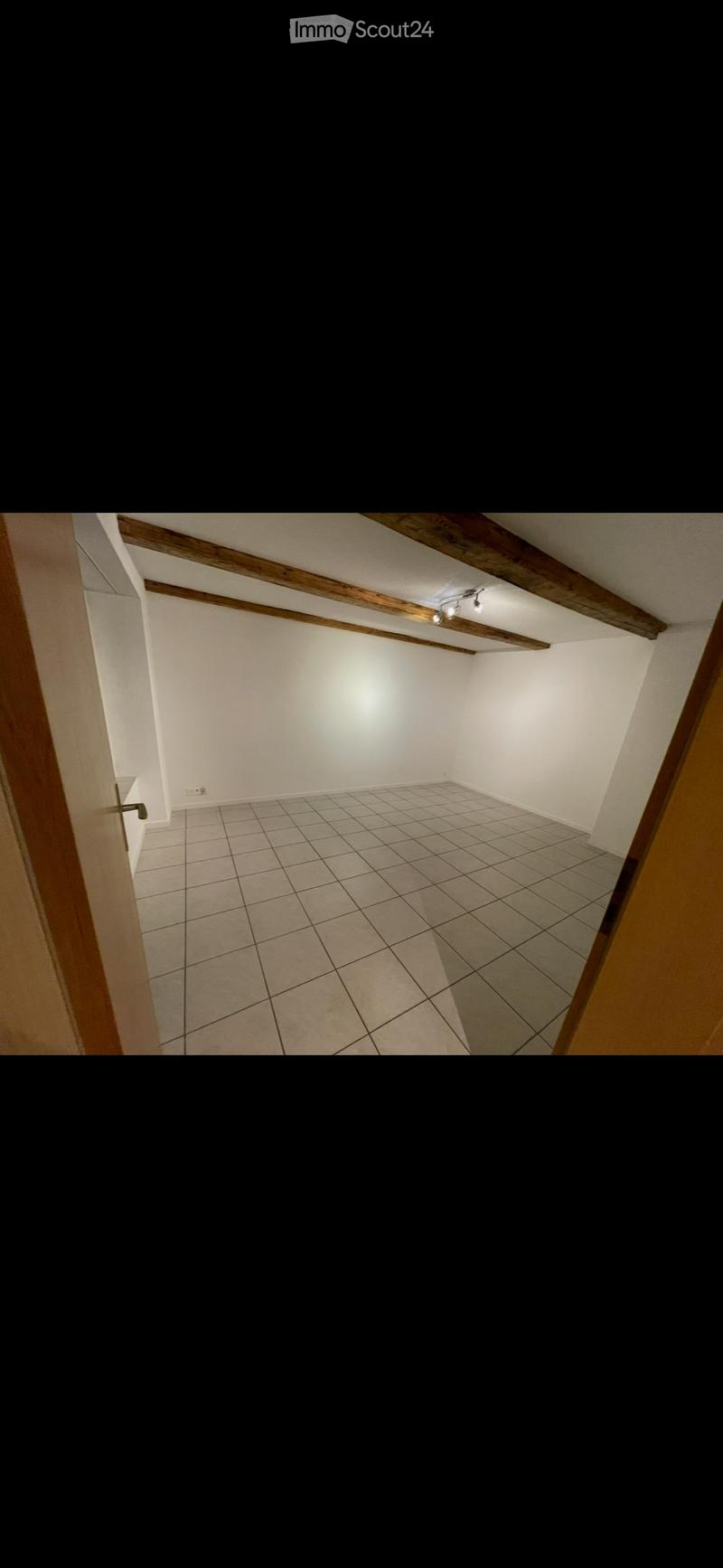 Empty room with tiled floor, white walls, wooden beams on the ceiling, and a single light fixture.