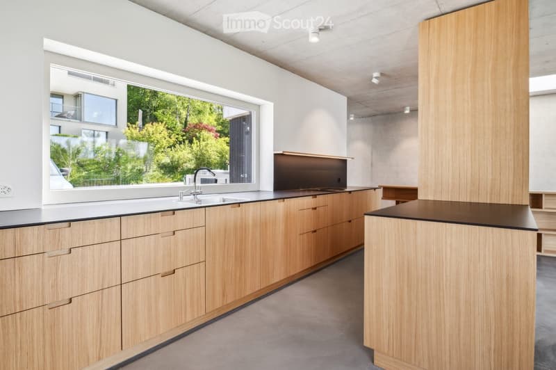 Empty room with concrete floor and white walls, large sliding glass doors leading to a balcony with a scenic view of green fields and trees.