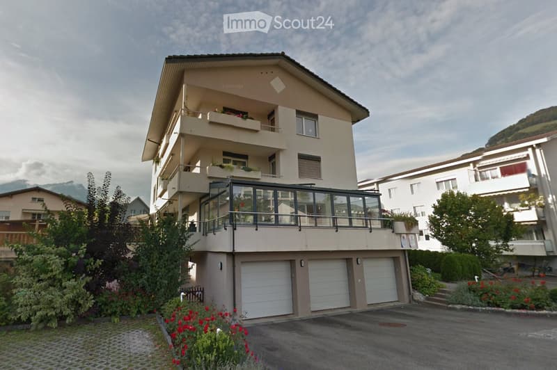 Multi-story residential building with beige facade, multiple balconies, and a garage area at the base.