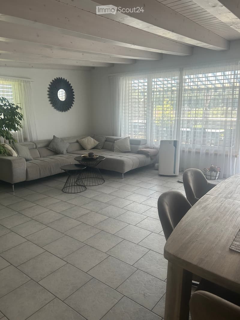 Living room with a grey sectional sofa, coffee table, dining table with chairs, air purifier, and a decorative mirror on the wall.