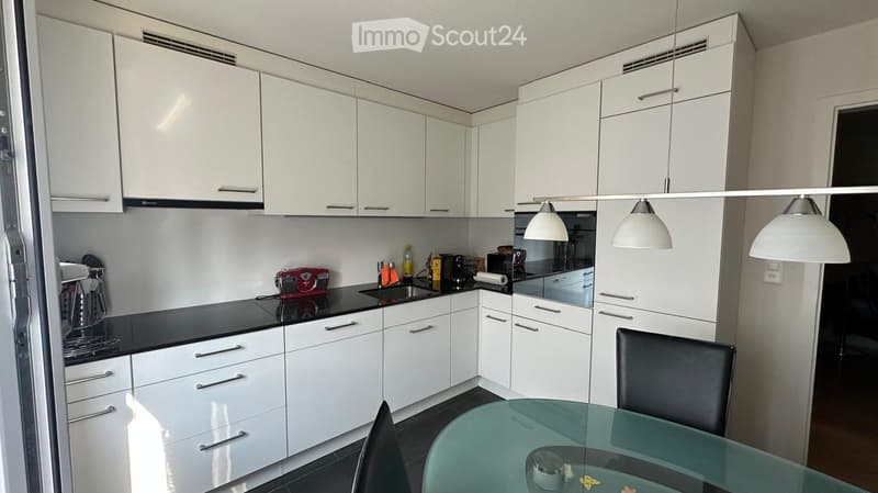 Modern kitchen with white cabinets, black countertops, and stainless steel appliances. Features a glass dining table with chairs, a coffee maker, and a toaster on the counter.