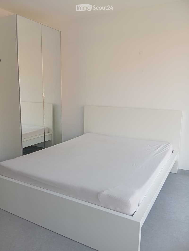Modern bedroom with a white bed, sleek headboard, and matching wardrobe with mirrored doors.