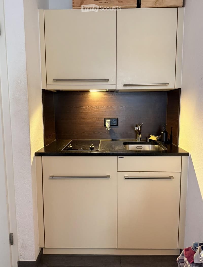 Modern kitchen with white cabinets, black countertop, built-in stove, and stainless steel sink.