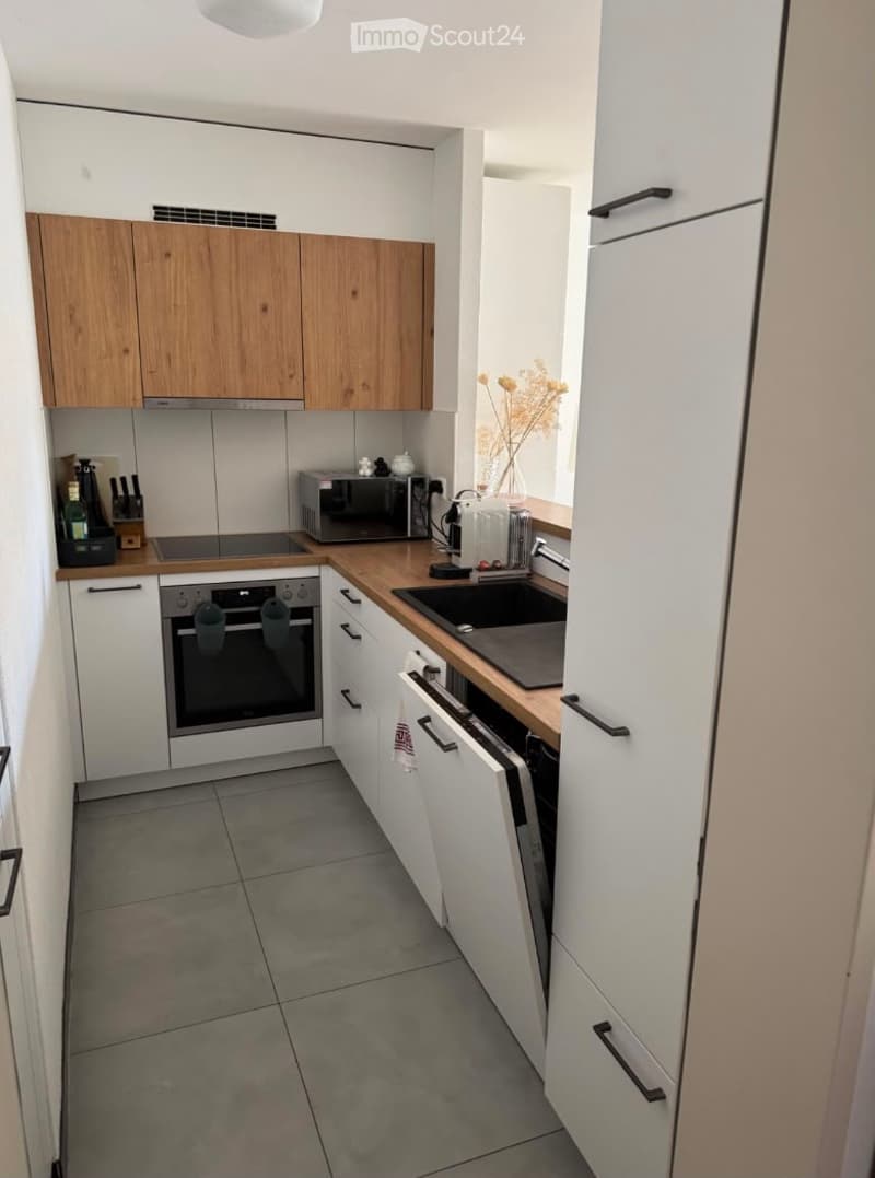 Modern kitchen with white and wooden cabinets, stainless steel appliances, and a grey tiled floor.