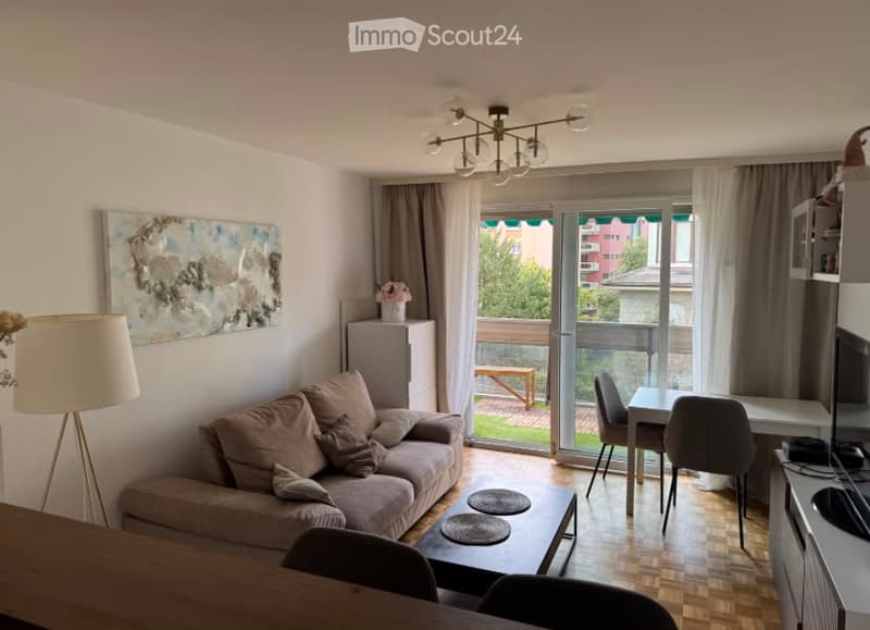A modern, open-concept living and dining area with a sofa, coffee table, dining table, chairs, and a balcony with outdoor furniture visible through large glass doors.