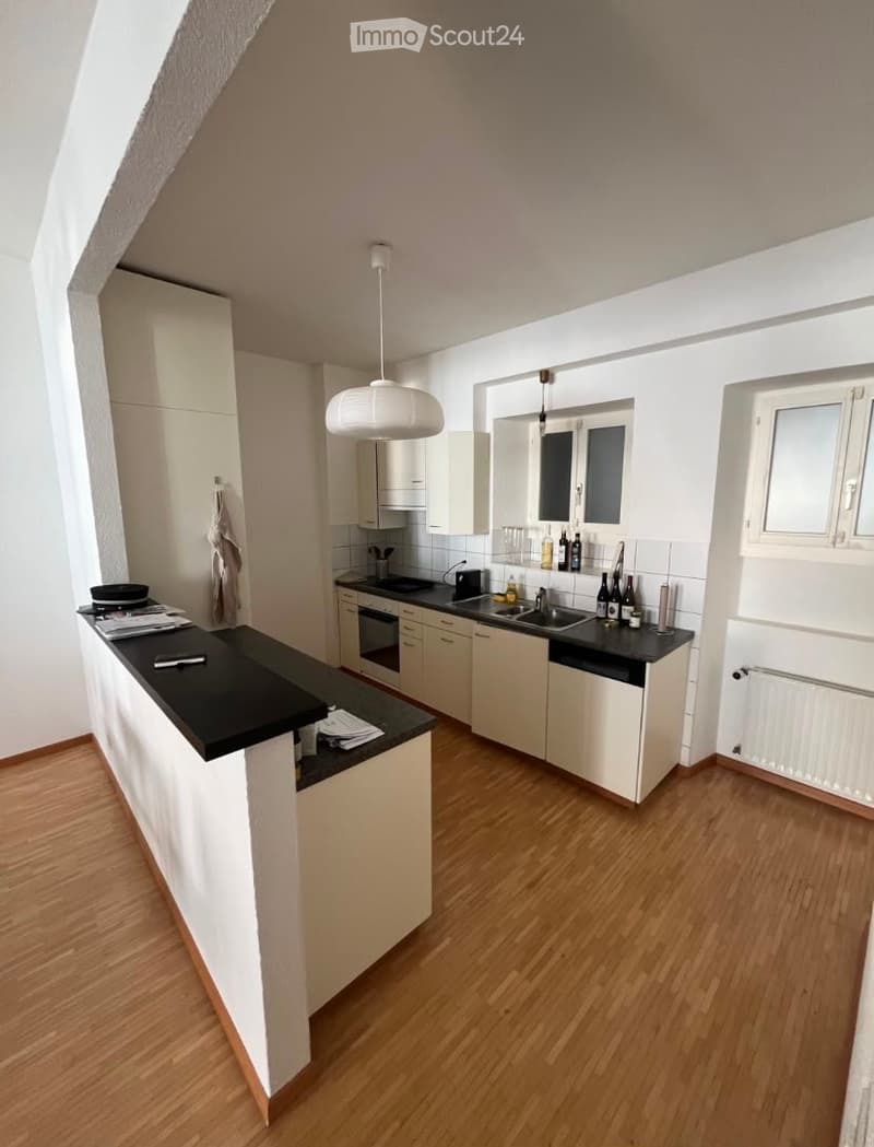 Modern kitchen with white cabinets, black countertops, wooden flooring, and a central island. Includes a sink, oven, and various kitchen items on the counter.