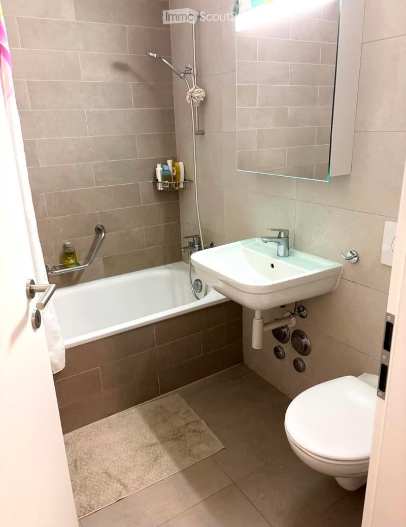 Modern bathroom with a bathtub, sink, toilet, and shower. Features a large mirror, tiled walls, and a towel on the floor.