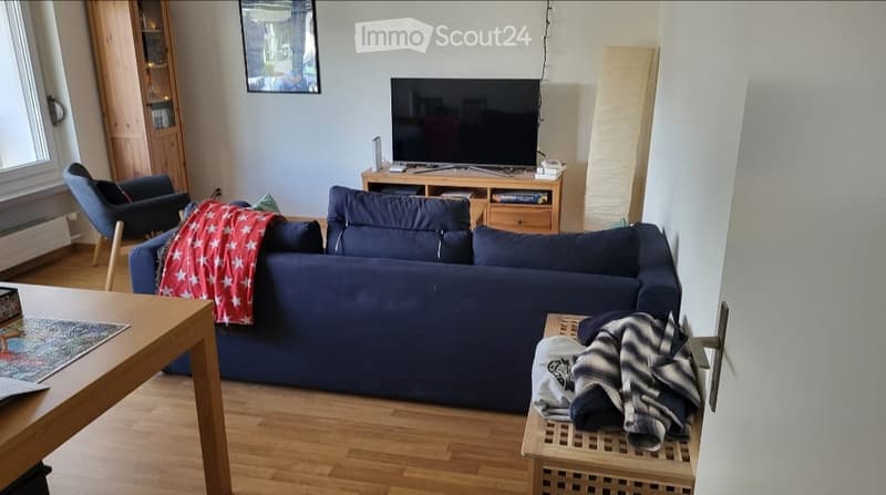 Living room with a blue sectional sofa, coffee table, TV stand, and a wooden table with a map on it. There is a blue armchair and a small wooden shelf with books and a mirror on the wall.