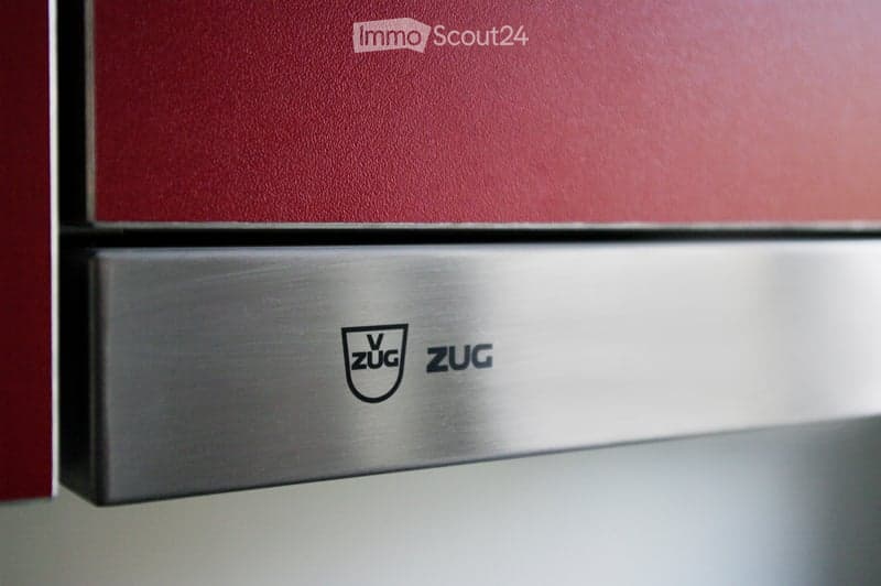 Close-up of a stainless steel dishwasher with the brand name "ZUG" visible on the handle.