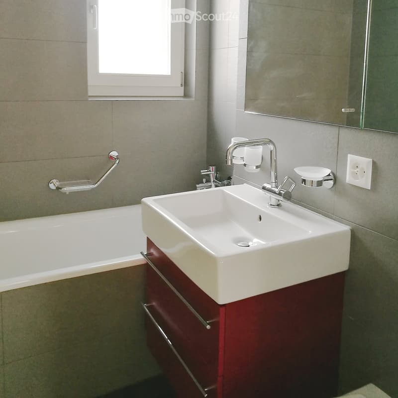Modern bathroom with a white bathtub, a double sink with chrome faucet, and a dark red cabinet beneath the sink.