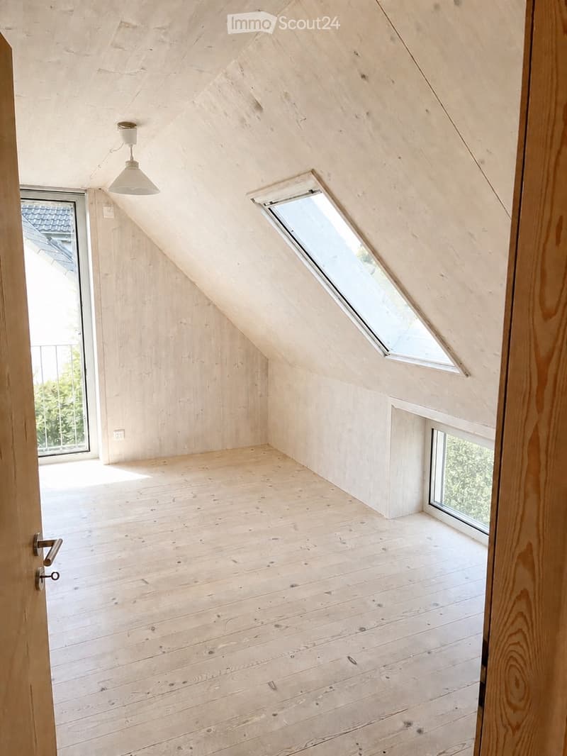 Empty attic room with wooden walls, floor, and ceiling, featuring skylight windows and a hanging light fixture.