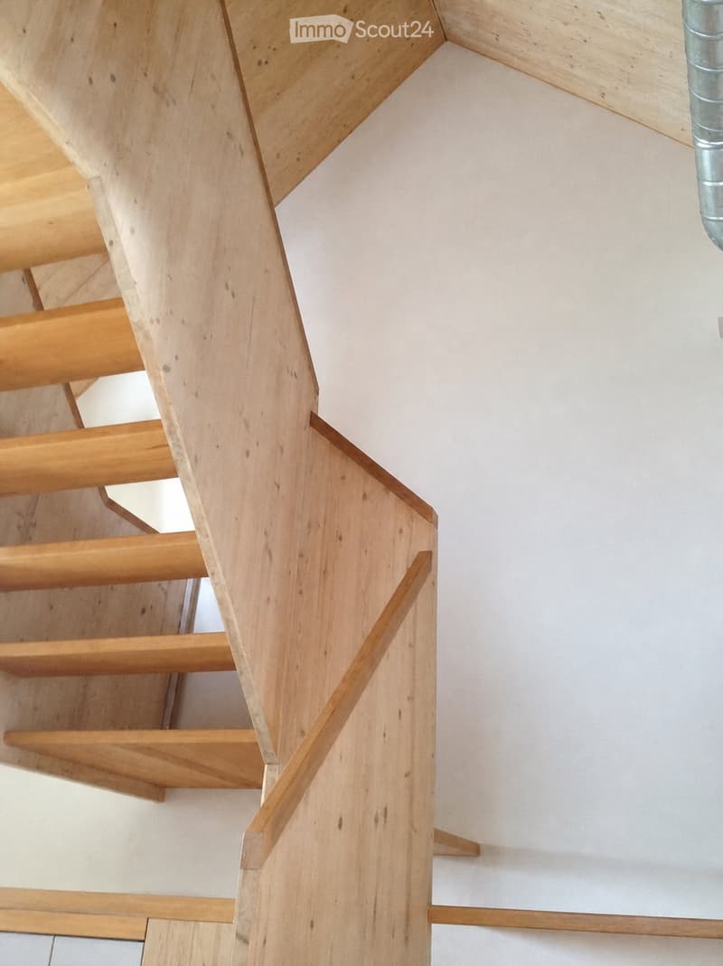 Modern wooden staircase with open risers and handrails, white walls, and a visible metal pipe on the right side.
