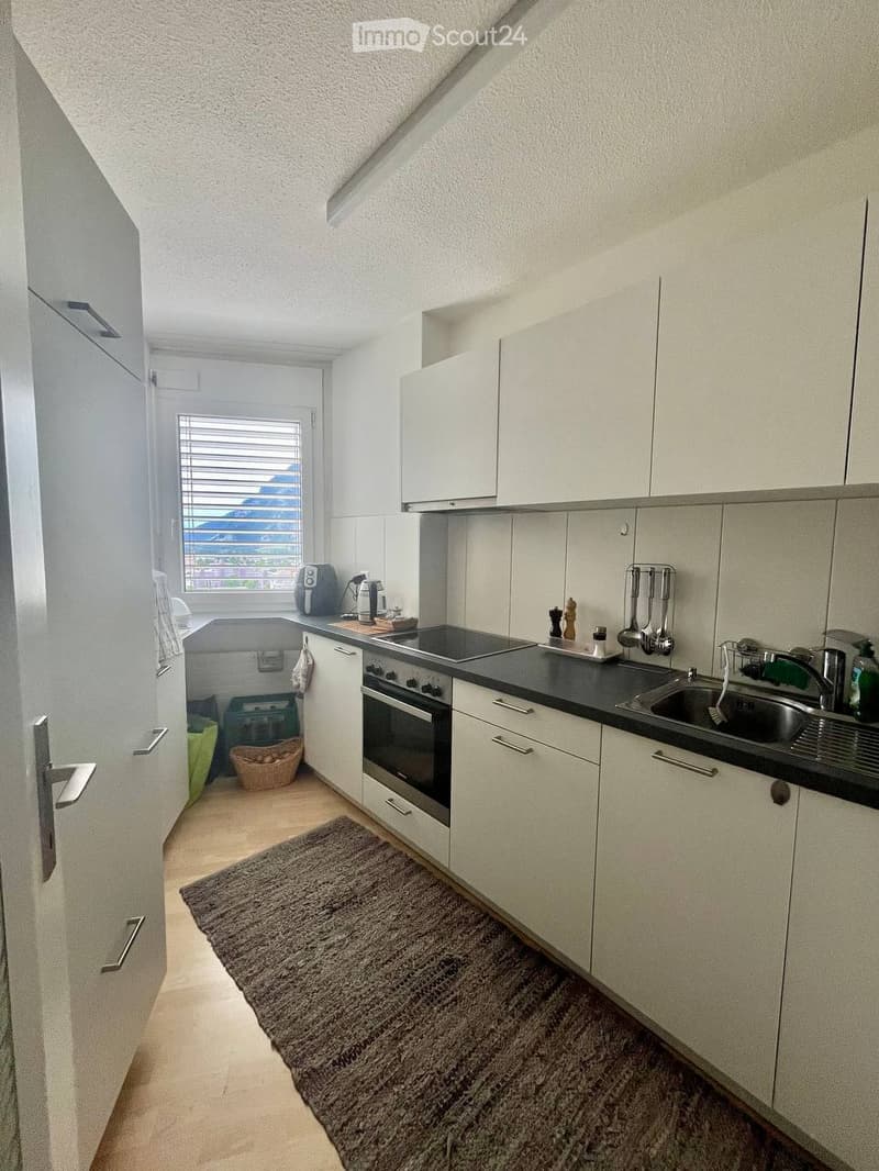 Modern kitchen with white cabinets, stainless steel appliances, and a black countertop. Features include an oven, sink, coffee maker, and various kitchen utensils.