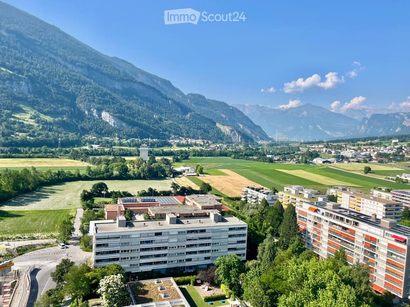 Aerial view of a residential complex surrounded by green fields and mountains in the background.