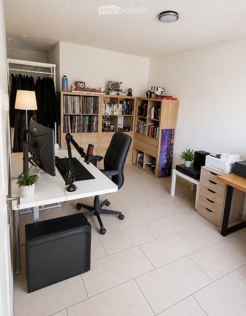 A modern, well-organized home office with a white desk, ergonomic chair, large screen, keyboard, bookshelf filled with books and decorative items, a small potted plant, and a lamp. The room features tiled flooring and a built-in closet with hanging clothe
