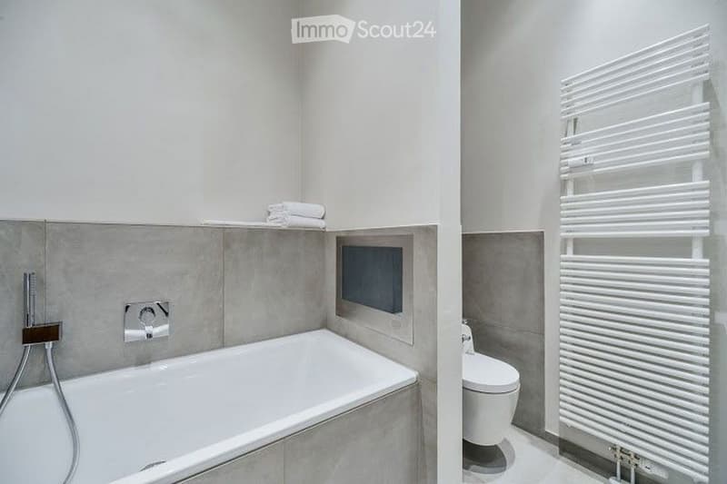 Modern bathroom with a bathtub, toilet, towel rack, and neatly folded towels on a shelf.
