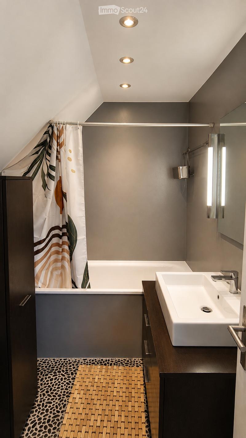 Modern bathroom with a bathtub, sink, mirror, and shower curtain. Features a dark wooden cabinet, a patterned floor, and recessed ceiling lighting.