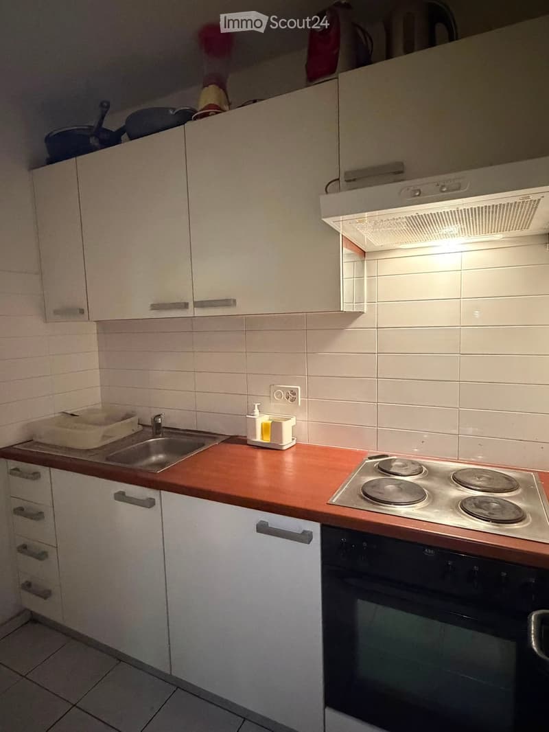 Modern kitchen with white cabinets, a stainless steel sink, a four-burner electric stove, and an oven. The countertops are a warm reddish-brown wood, and the backsplash is white tiles.