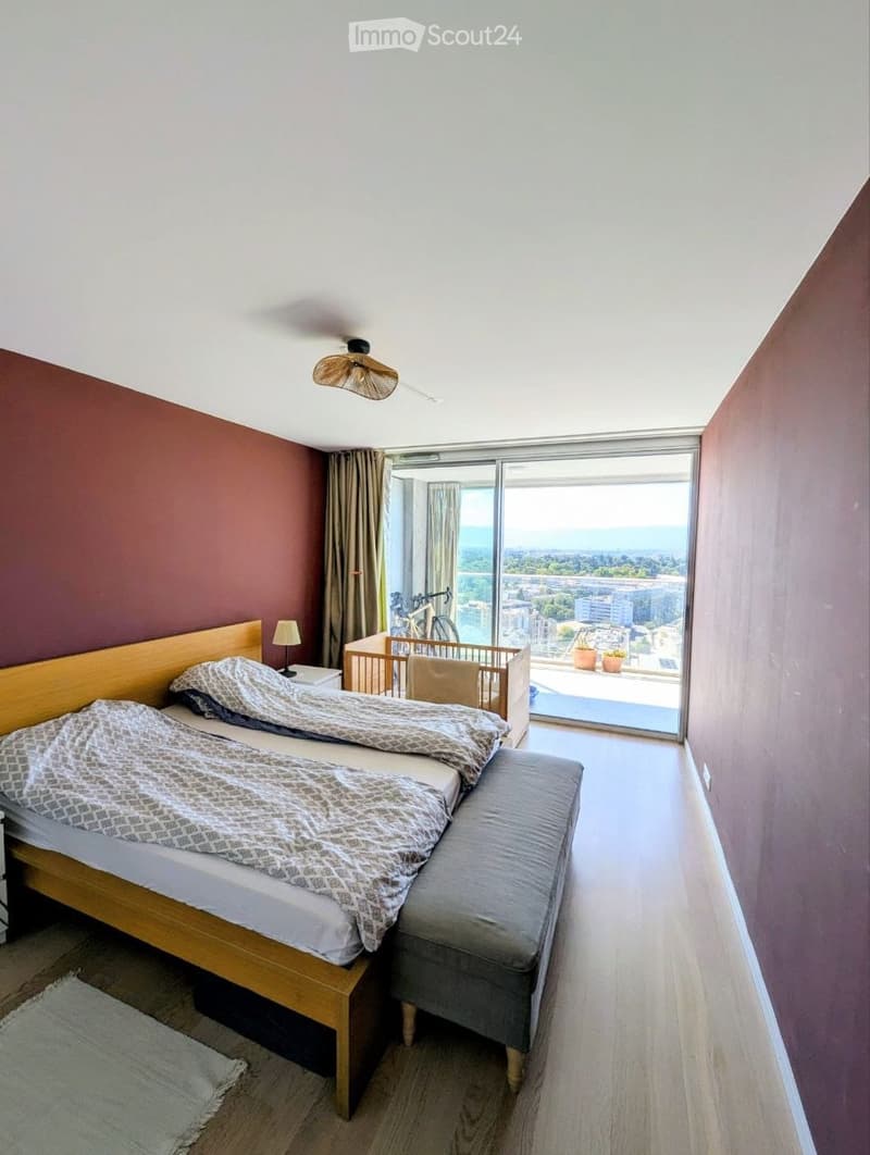 Modern bedroom with two single beds, nightstand, lamp, baby crib, sofa, and a view of the city and ocean through large windows.