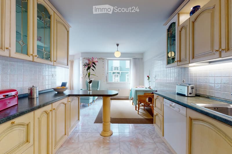 Bright kitchen with light-colored cabinets, granite countertops, and a central island. Includes a toaster, dishwasher, and a small seating area with a table and chairs.
