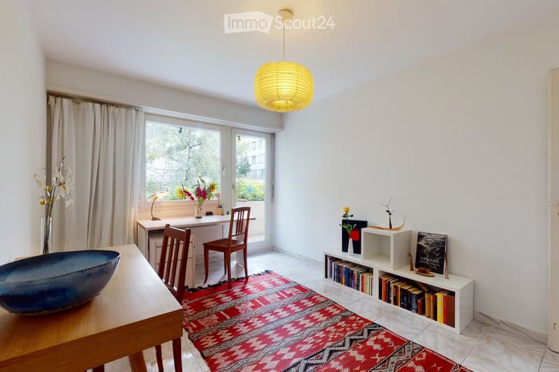 Bright, modern room with a wooden table, chairs, bookshelf, decorative vase, and a large window with a view of greenery.