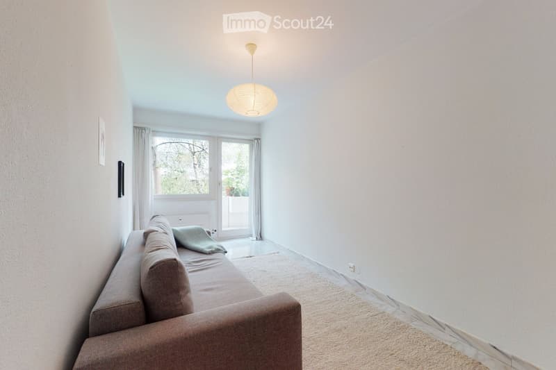 Modern living room with a grey sectional sofa, a pendant light fixture, and a large window with a sliding glass door leading to a balcony.