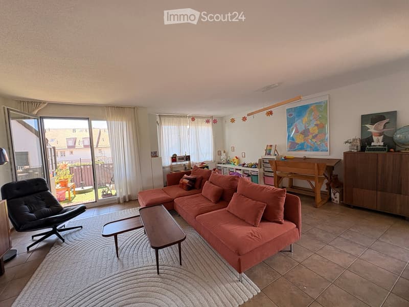 Bright living room with a red sectional sofa, coffee table, armchair, and a view of the garden through large windows.