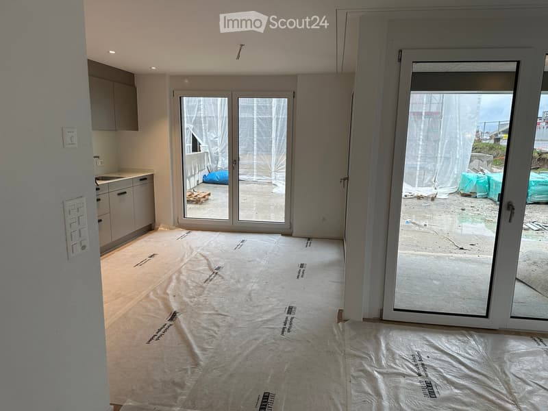 Empty room with bare walls, covered floor, and large glass doors leading to an outdoor area.