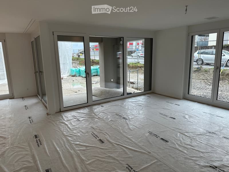 Empty room with white walls, large sliding glass doors, and protective plastic sheeting on the floor.