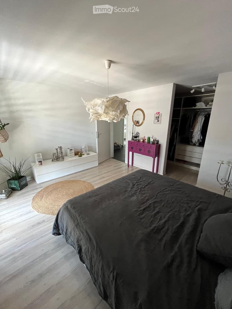 Modern bedroom with a large bed, white nightstand, pink dresser, round woven rug, and a hanging paper lamp.